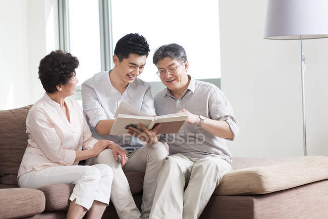 Chinesisches Seniorenpaar mit erwachsenem Sohn schaut sich Fotoalbum an — Stockfoto