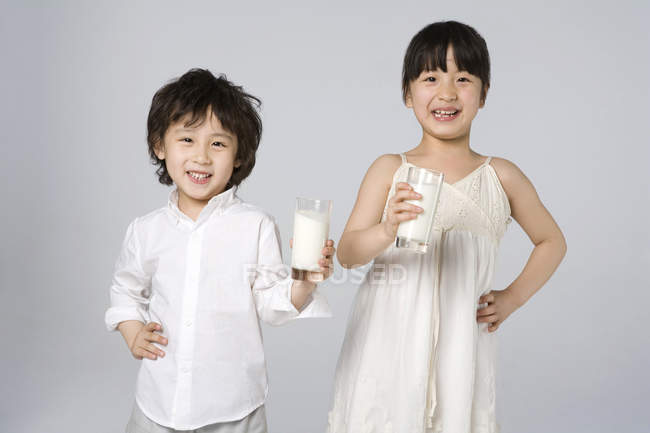 Азиатские дети держат стаканы молока на сером фоне — стоковое фото