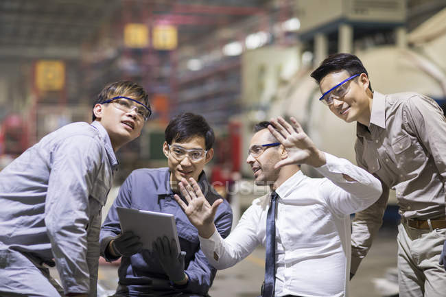 Businessman and Asian engineers using digital tablet and talking at factory — Stock Photo