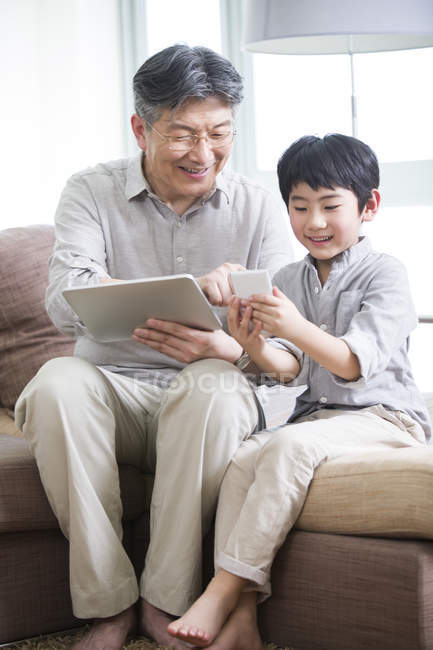 Китайський діда і онука, використовуючи цифровий планшет і смартфон на дивані — стокове фото