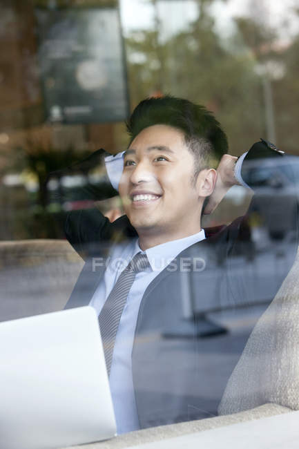 Hombre de negocios chino sentado con las manos detrás de la cabeza en la cafetería - foto de stock