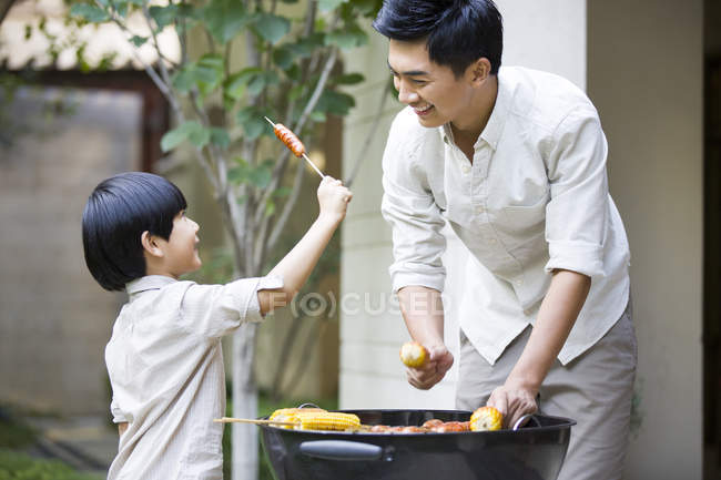 Chinese father and son barbecuing in courtyard — Stock Photo