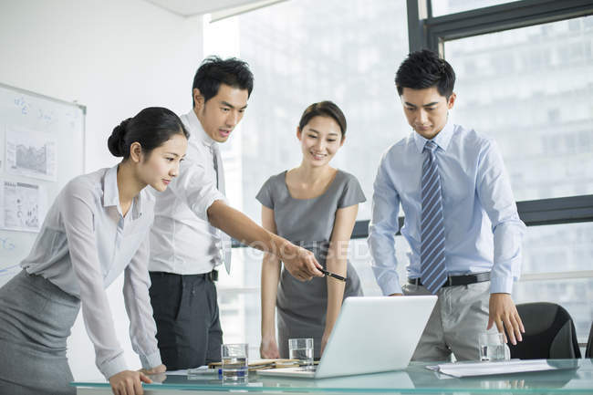Chinese business team talking in meeting and pointing at laptop — Stock Photo