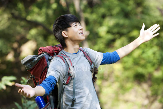 Chinese hiker with arms outstretched looking up in forest — Stock Photo