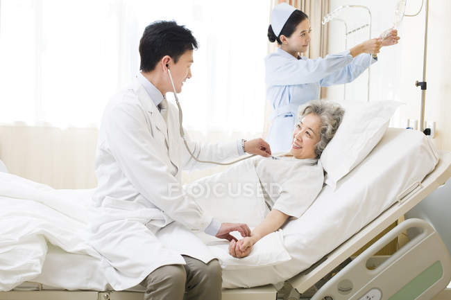 Chinese doctor using stethoscope on patient in hospital — Stock Photo