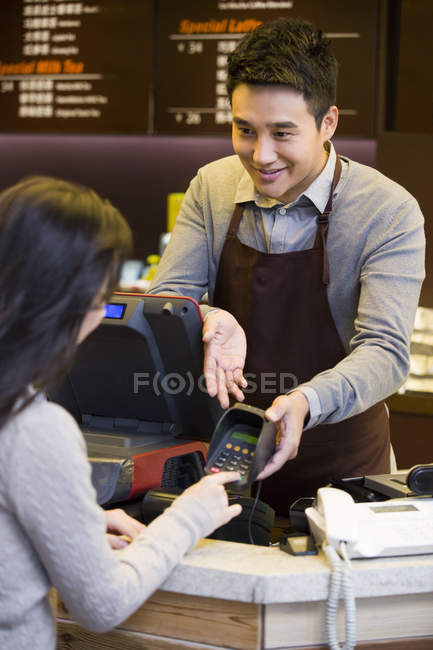 Cliente chino ingresando contraseña de tarjeta de crédito en el mostrador de café - foto de stock