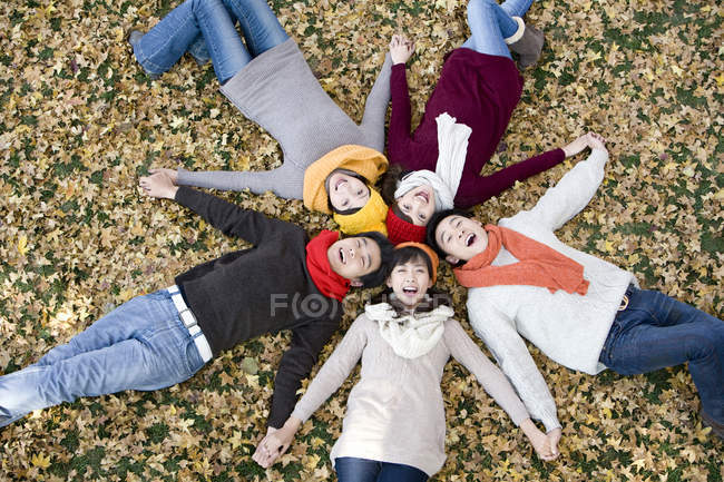 Amigos chinos tumbados en forma de estrella tomados de la mano en el parque - foto de stock