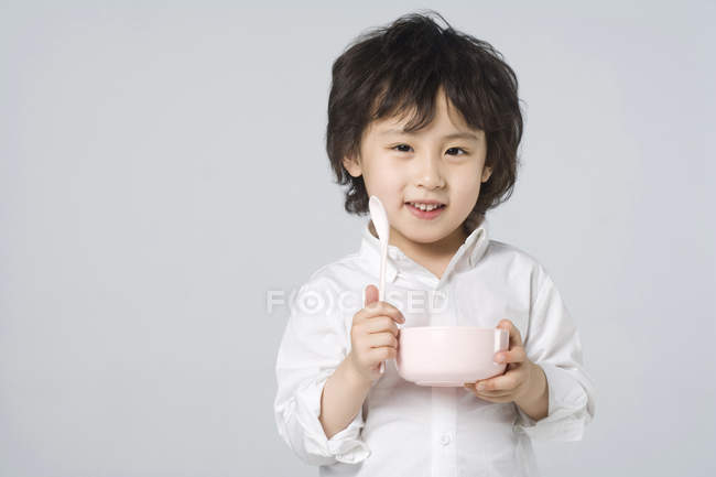 Маленька азіатських хлопчика, що тримається миски і ложки на сірий фон — стокове фото