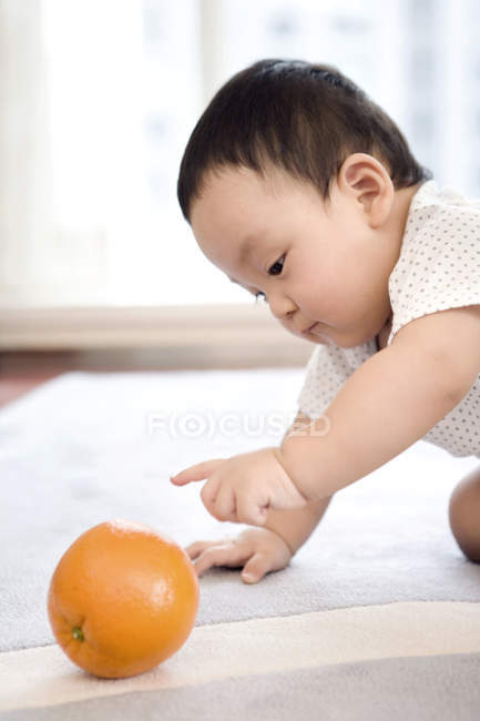 Menino chinês rastejando e brincando com frutas laranja — Fotografia de Stock