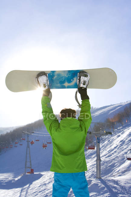 Вид ззаду чоловіка позує зі сноубордом на гірськолижному курорті — стокове фото