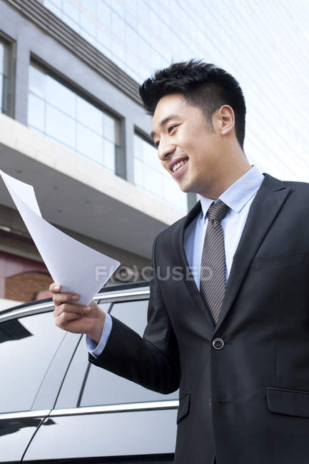 Hombre de negocios chino sosteniendo archivo delante del coche - foto de stock