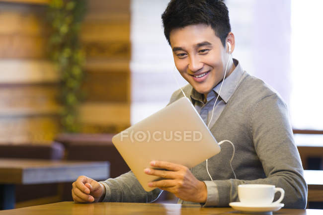 Hombre chino mirando hacia abajo en la tableta digital en la cafetería - foto de stock