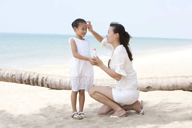 Mãe chinesa aplicando creme solar na filha — Fotografia de Stock