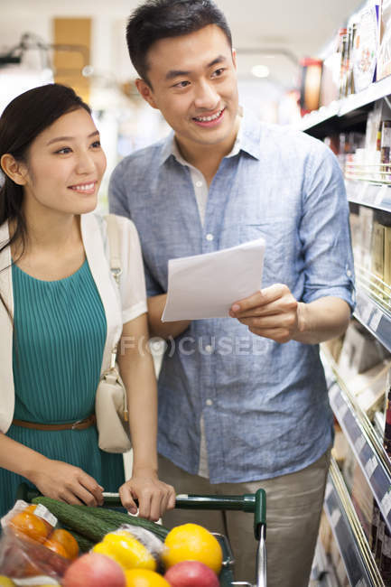 Pareja china celebración de la lista de compras en el supermercado - foto de stock