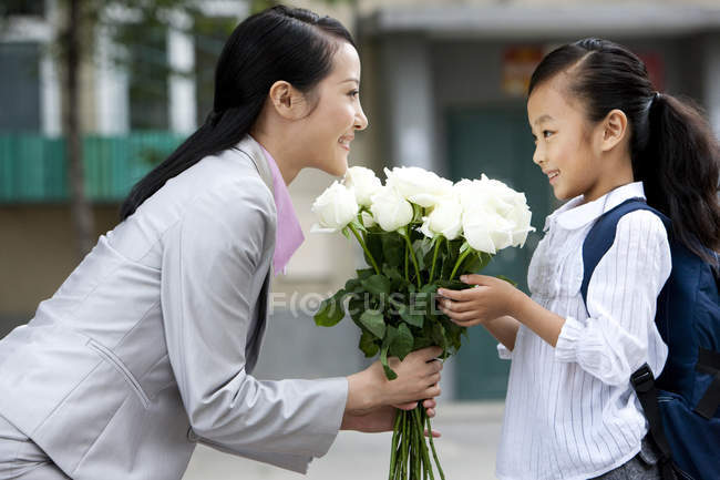 Chinese schoolgirl offering mother bunch of flowers — Stock Photo