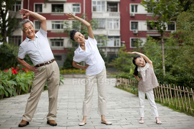 Chinese girl exercising with grandparents on street — Stock Photo