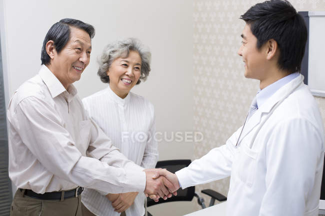 Casal sênior chinês apertando as mãos com o médico no hospital — Fotografia de Stock