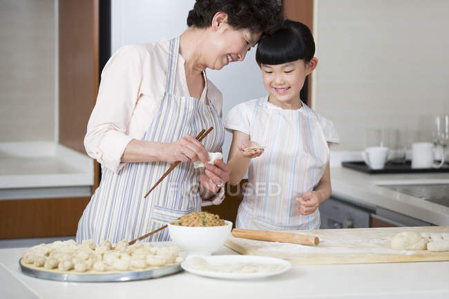 Chinese grandmother and granddaughter making dumplings in kitchen — Stock Photo