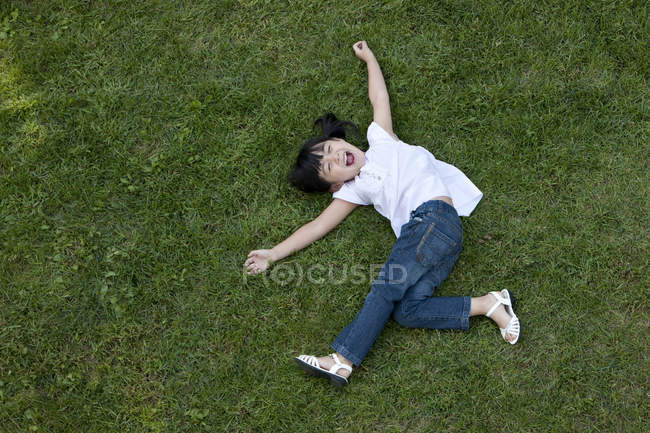 Extático menina chinesa deitada na grama verde — Fotografia de Stock