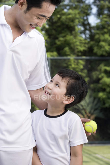 Padre chino abrazando hijo en cancha de tenis - foto de stock