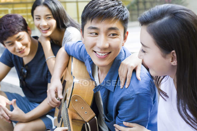 Hombre chino tocando la guitarra con amigos en la calle - foto de stock