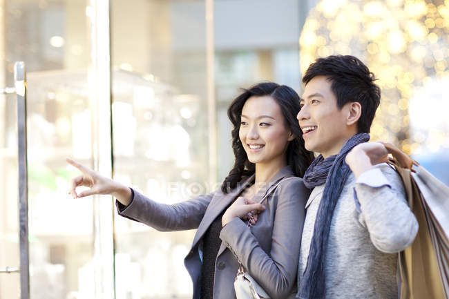 Mujer china apuntando a la ventana de la tienda mientras pasea con el hombre - foto de stock