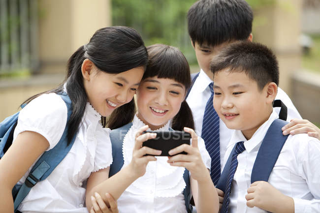 Los escolares chinos utilizan smartphone en el patio de la escuela - foto de stock