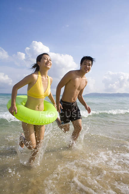 Молода пара біжить з надувним кільцем у морській воді — стокове фото