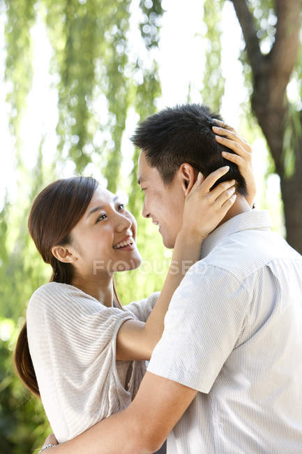 Joven pareja china abrazándose bajo el sauce en el parque - foto de stock