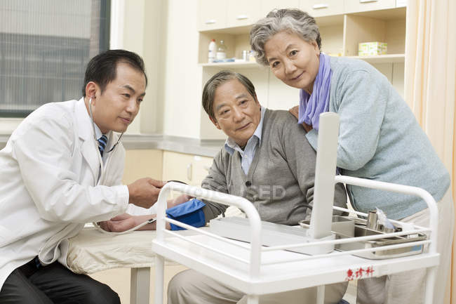 Chinese doctor testing senior man blood pressure — Stock Photo