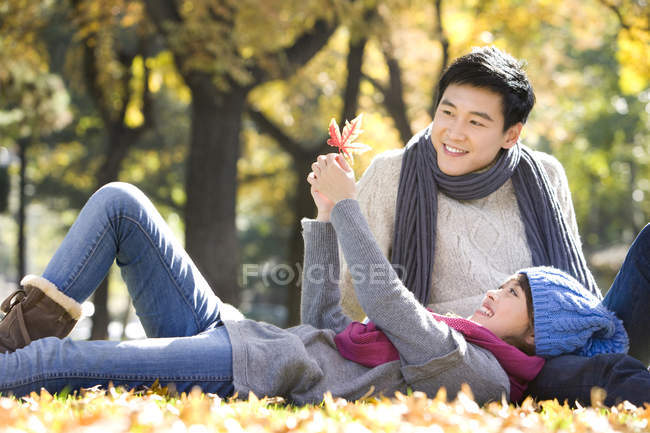 Chinese couple lying on ground and looking at maple leaf in park — Stock Photo