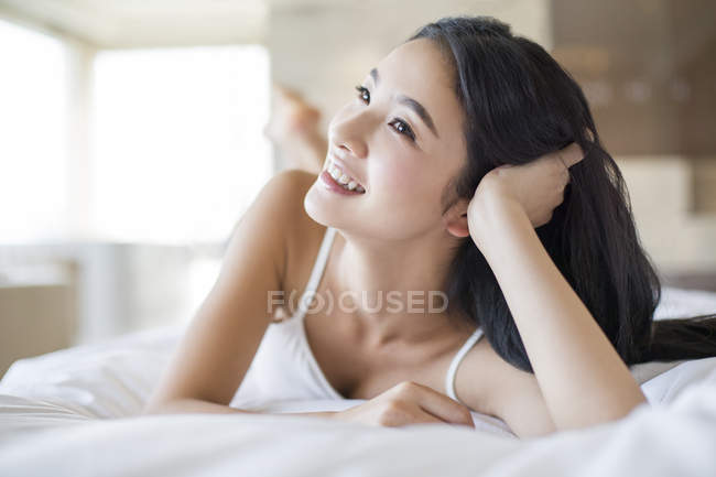 Mujer china acostada en la cama y apoyándose en el codo - foto de stock