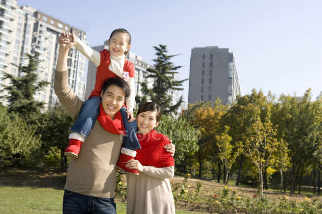 Chinese father carrying daughter on shoulders with mother in park — Stock Photo