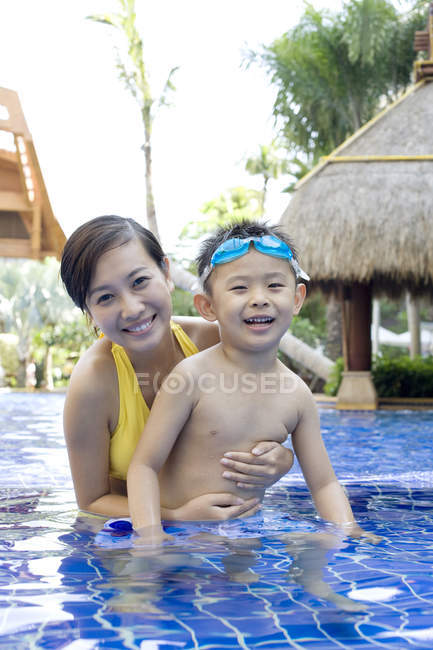 Chino madre e hijo divirtiéndose y mirando en cámara en piscina - foto de stock