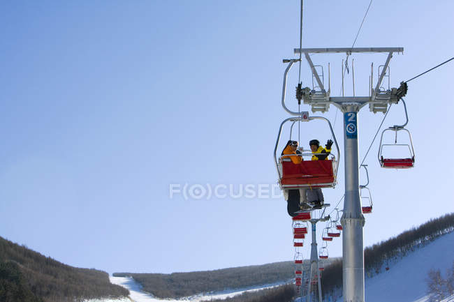Chinese couple using ski lift at winter resort — Stock Photo