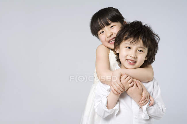 Asiático irmão e irmã abraçando em fundo cinza — Fotografia de Stock