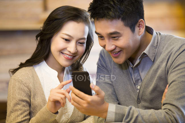 Chinese couple using smartphone together in cafe — Stock Photo