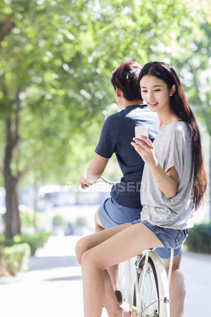 Femme chinoise assise sur petit ami vélo avec smartphone — Photo de stock