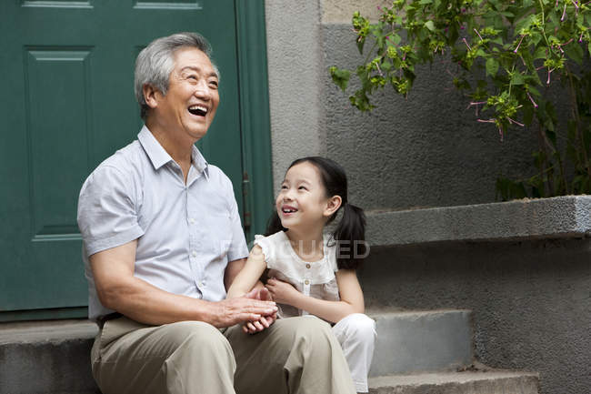 Chinese grandfather and granddaughter laughing on porch — Stock Photo
