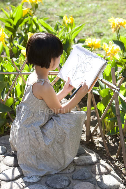 Kleines Mädchen zeichnet gelbe Blumen im Garten — Stockfoto