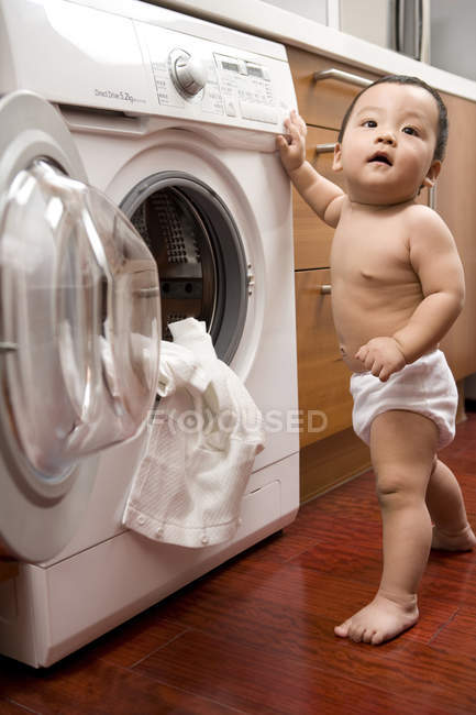 Bebé chino de pie y aferrado a la lavadora - foto de stock