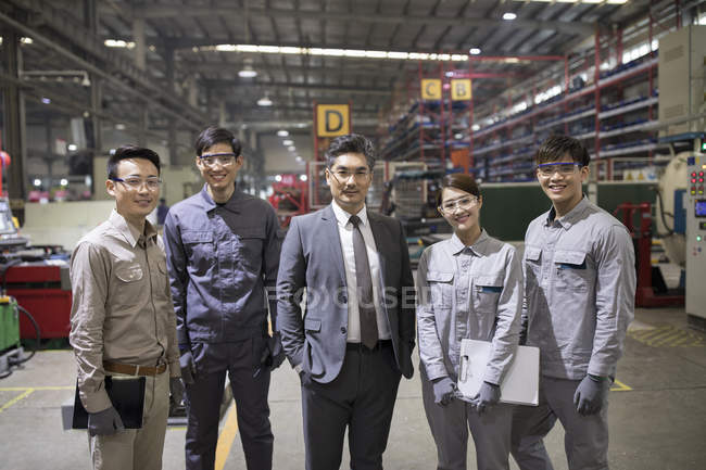 Mature Chinese businessman and engineering team posing at factory — Stock Photo