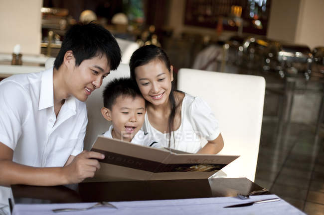 Genitori cinesi e figlio guardando attraverso il menu nel ristorante — Foto stock