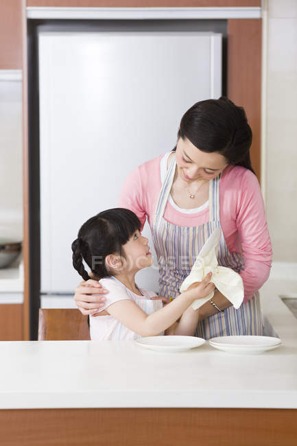 Chinese girl drying plates with mother in kitchen — Stock Photo
