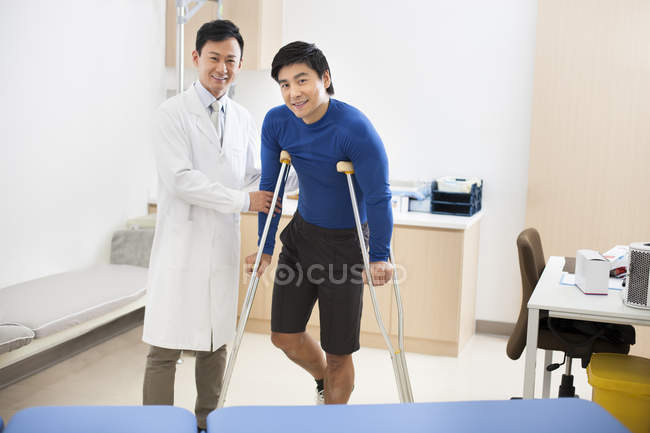 Chinese doctor helping patient with crutches — Stock Photo