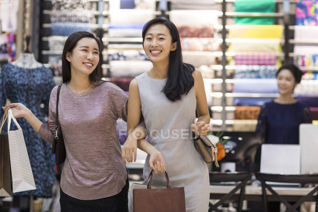 Chinas amigas caminando de la mano en la tienda de ropa - foto de stock