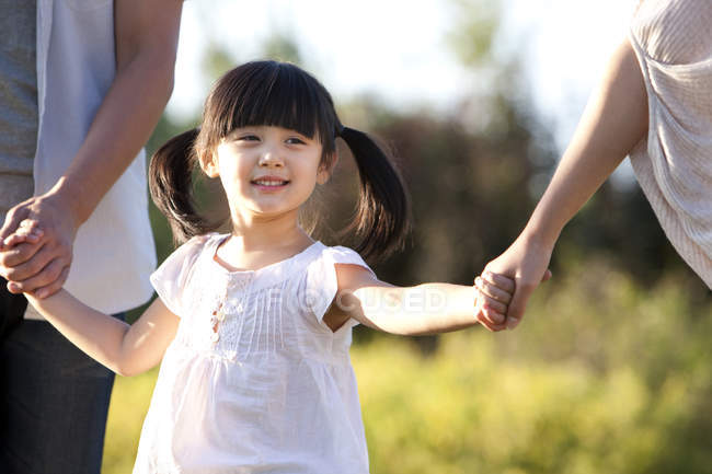 Petite fille chinoise avec des nattes tenant la main avec la famille dans la prairie d'été — Photo de stock