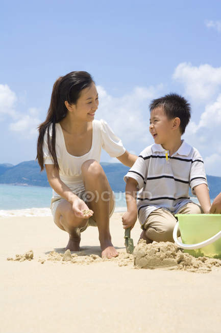 Madre e hijo jugando con arena en la playa - foto de stock