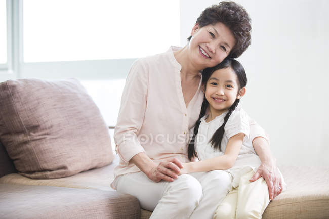 Cinese nonna e nipote abbracciare sul divano e guardando in macchina fotografica — Foto stock