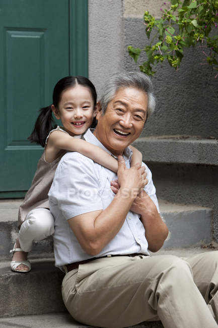 Abuelo y nieta chinos abrazándose en el porche - foto de stock